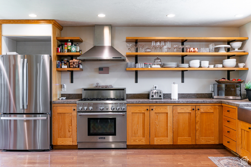 Kitchen featuring stainless steel appliances, wall chimney range hood, open shelves, light wood-style flooring, and recessed lighting