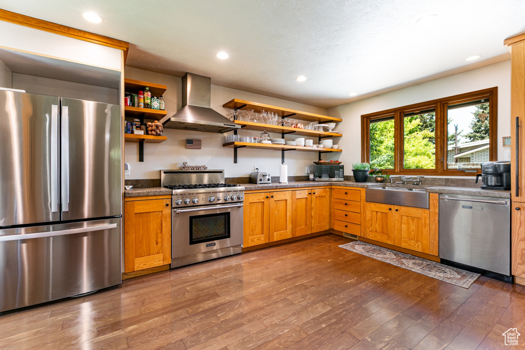 Kitchen featuring appliances with stainless steel finishes, wall chimney range hood, a sink, open shelves, and dark wood-style flooring