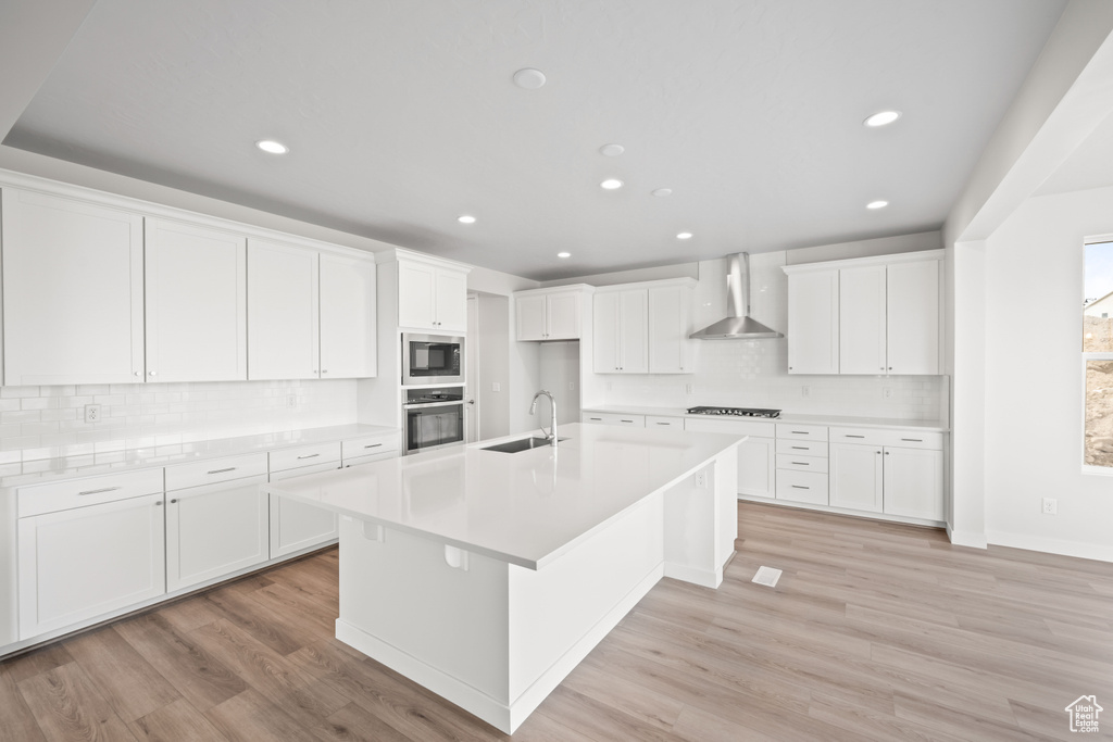 Kitchen featuring appliances with stainless steel finishes, wall chimney exhaust hood, decorative backsplash, a sink, and recessed lighting