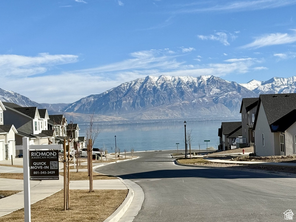 View of asphalt street with curbs, a water and mountain view, and sidewalks