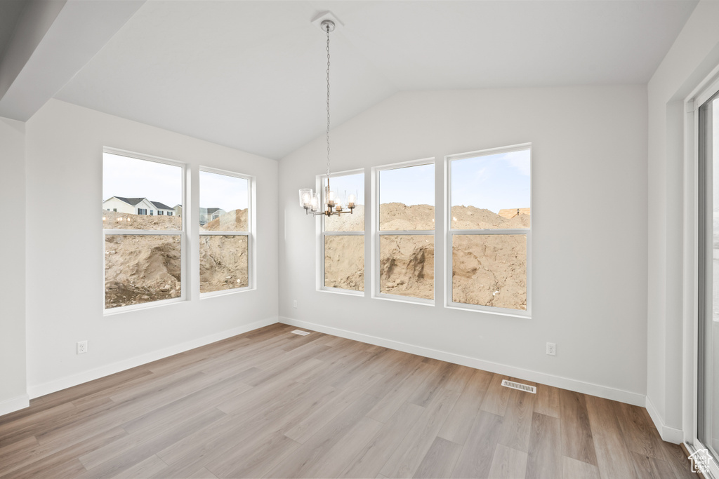 Unfurnished dining area with a chandelier, light wood finished floors, vaulted ceiling, and baseboards