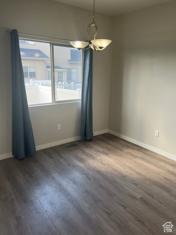 Spare room featuring dark wood-style flooring, baseboards, and a chandelier