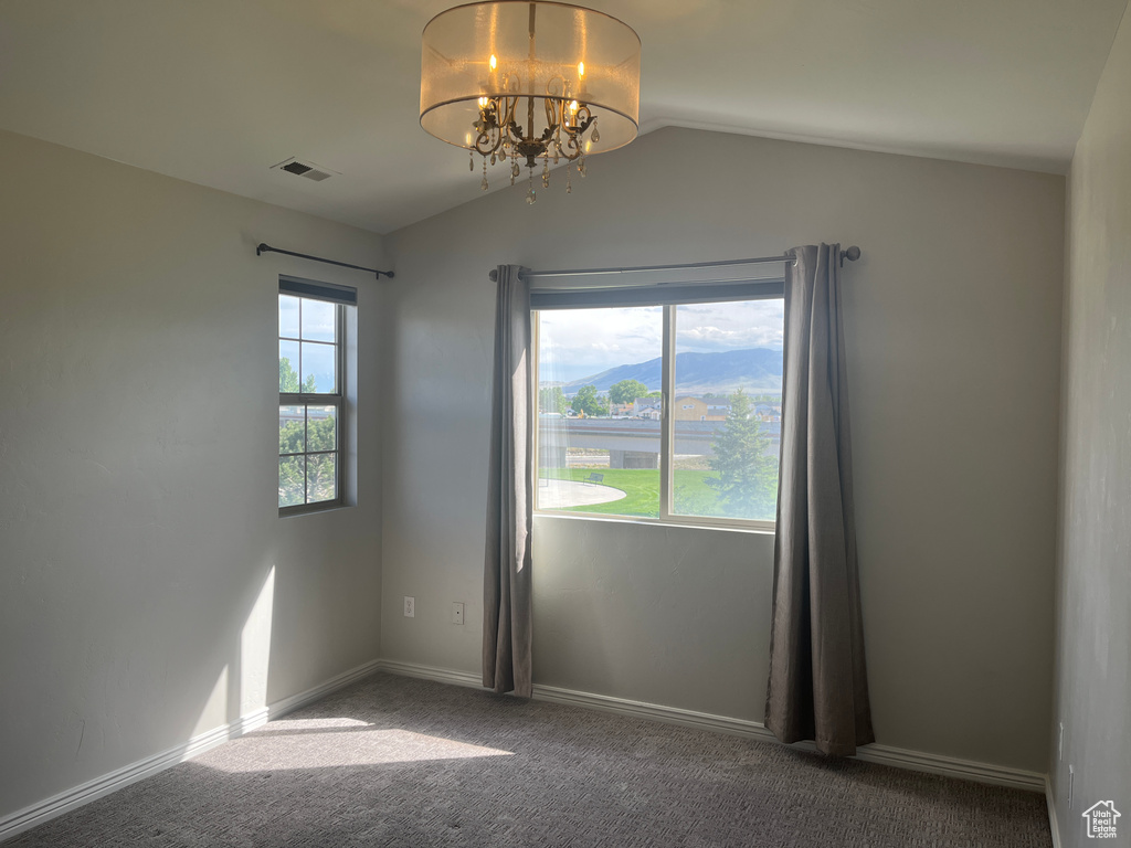 Carpeted spare room featuring vaulted ceiling, a chandelier, and baseboards
