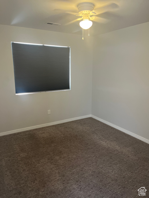 Empty room with a ceiling fan, baseboards, and dark colored carpet
