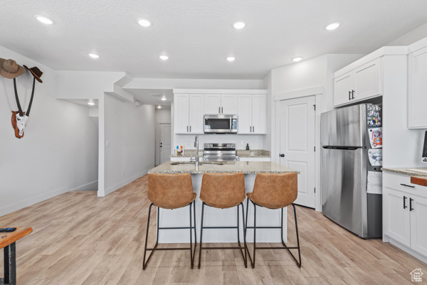 Kitchen with stainless steel appliances, a breakfast bar, white cabinetry, recessed lighting, and a sink