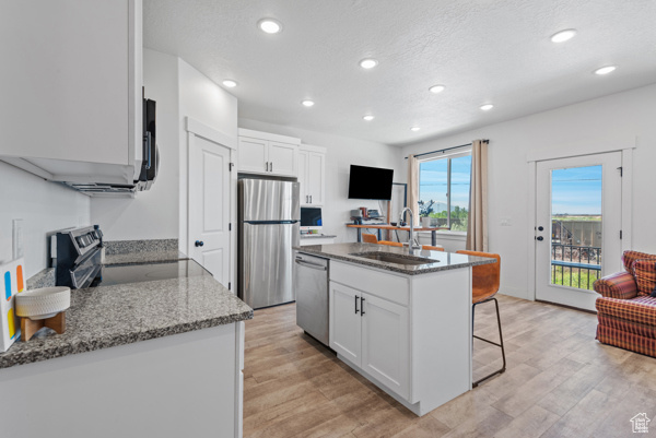 Kitchen with appliances with stainless steel finishes, a sink, recessed lighting, a breakfast bar, and light wood-style floors