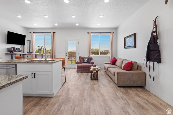 Living room with light wood-type flooring, recessed lighting, a textured ceiling, and baseboards