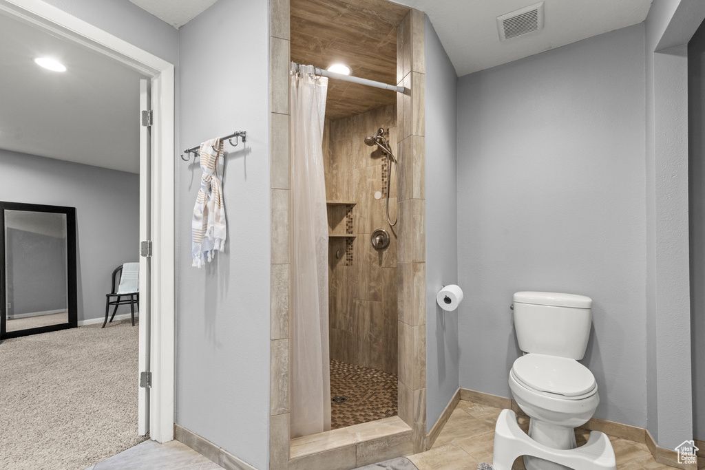 Bathroom with toilet, a tile shower, baseboards, and recessed lighting