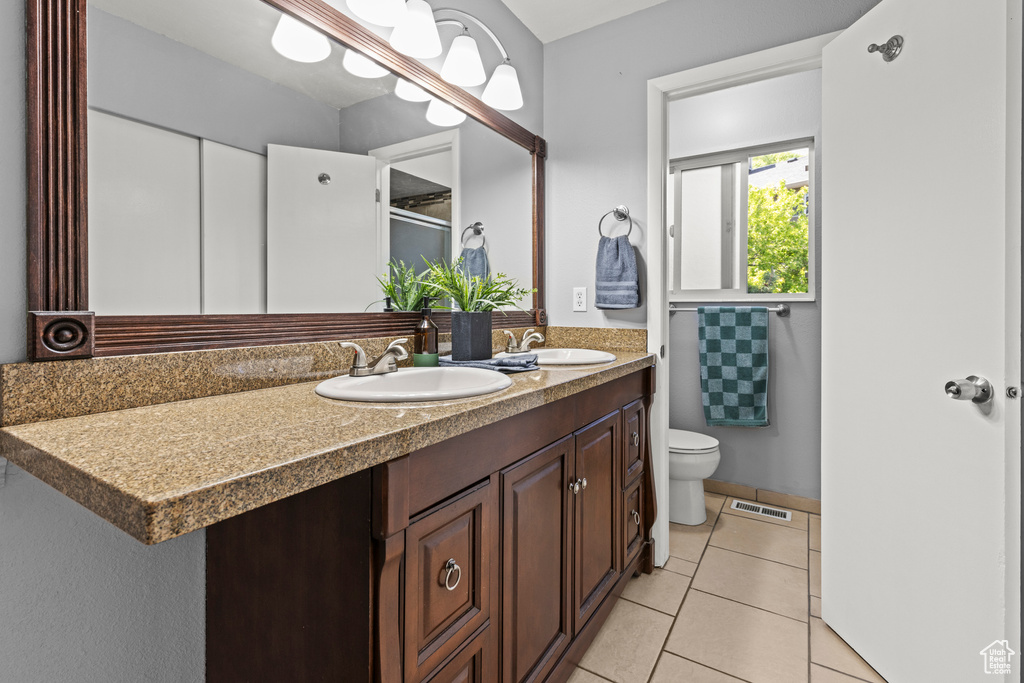 Full bathroom with double vanity, toilet, tile patterned floors, and a shower with door