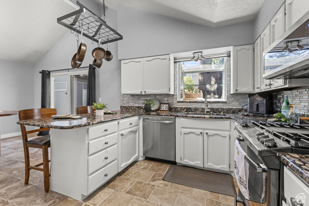Kitchen with stainless steel appliances, a peninsula, a sink, vaulted ceiling, and decorative backsplash
