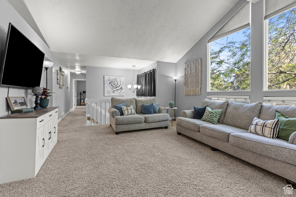 Living area with lofted ceiling, light colored carpet, and a chandelier