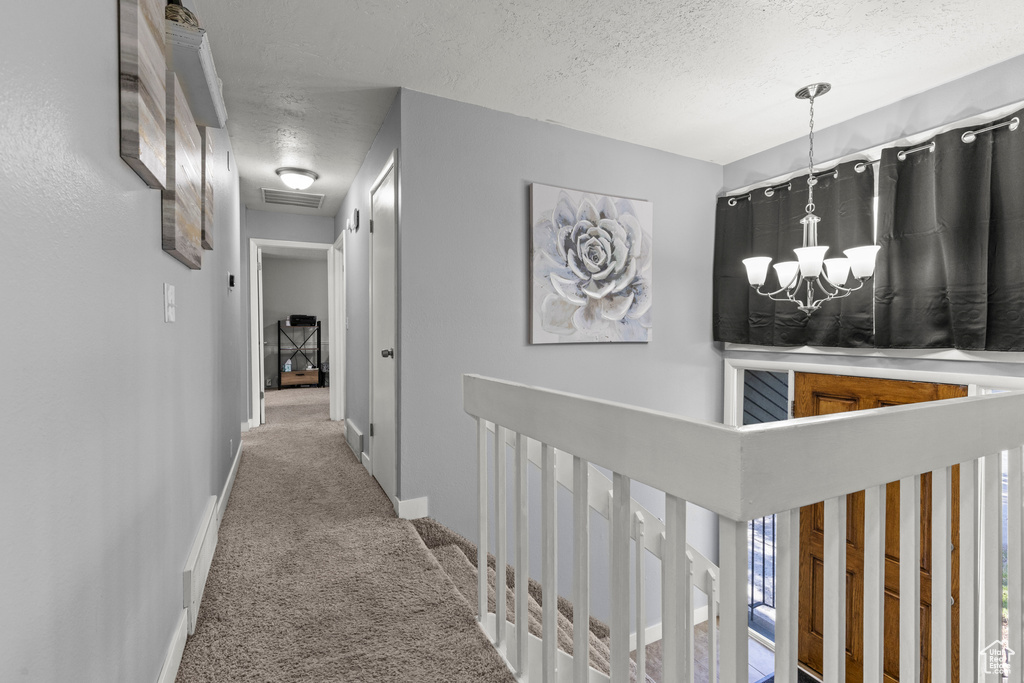 Hallway featuring carpet, a textured ceiling, a chandelier, an upstairs landing, and baseboards
