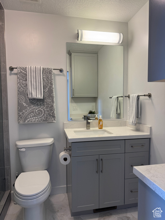 Full bathroom featuring marble finish floors, vanity, toilet, a stall shower, and a textured ceiling