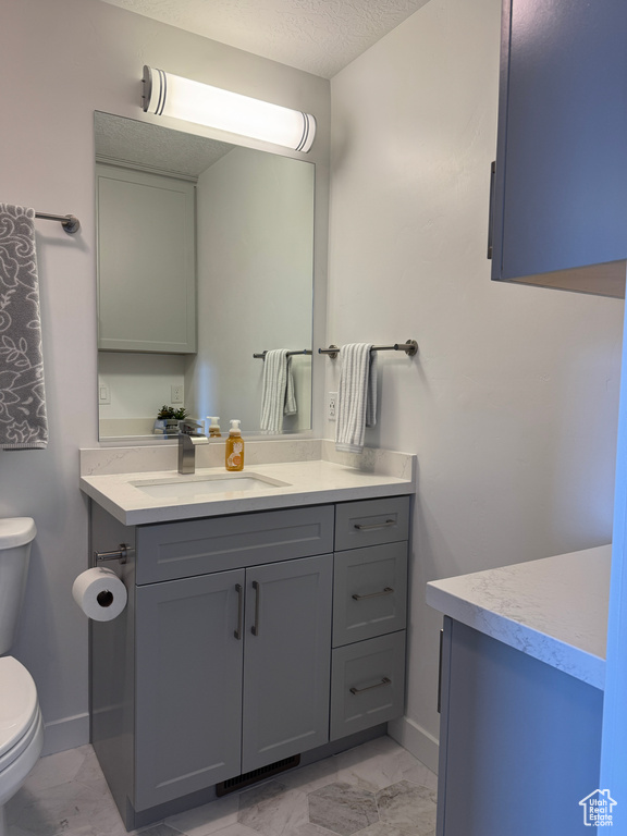 Bathroom featuring marble look tiles, toilet, vanity, baseboards, and a textured ceiling