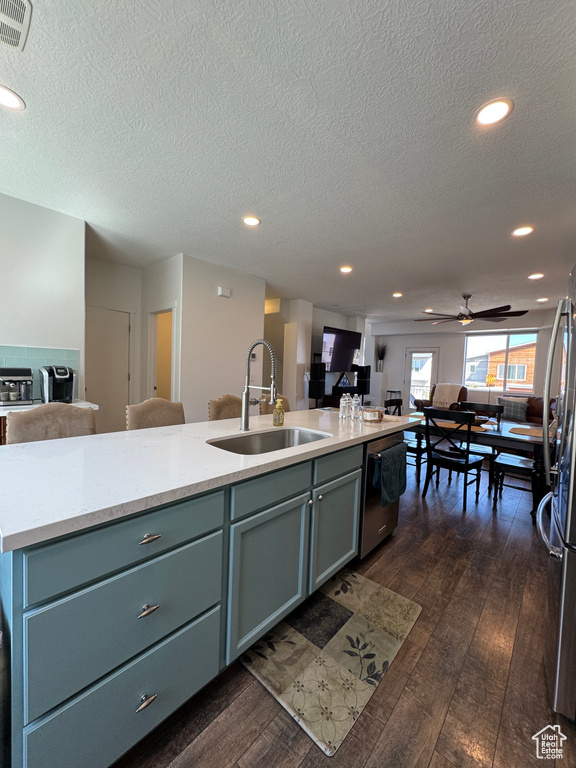 Kitchen with open floor plan, a sink, appliances with stainless steel finishes, dark wood-style flooring, and a kitchen island with sink