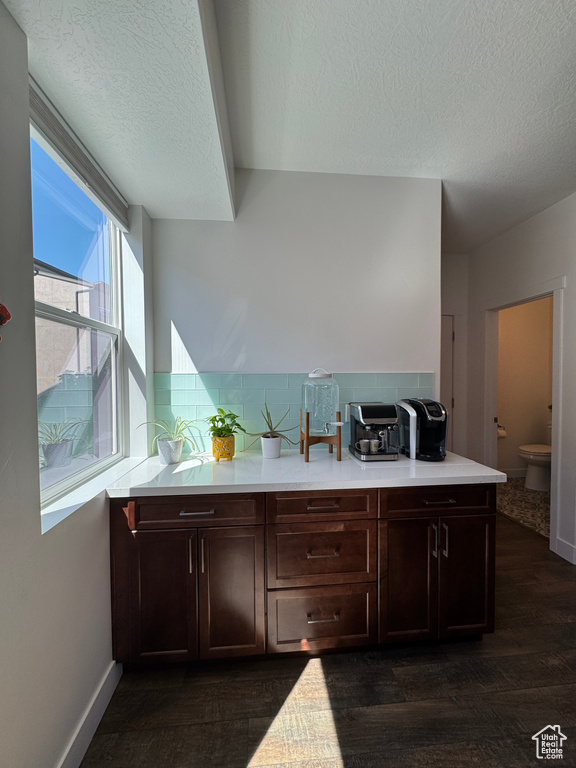 Kitchen featuring light countertops, dark wood-style floors, a textured ceiling, dark brown cabinets, and backsplash