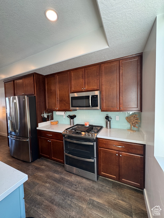 Kitchen featuring stainless steel appliances, a textured ceiling, light countertops, dark wood finished floors, and backsplash