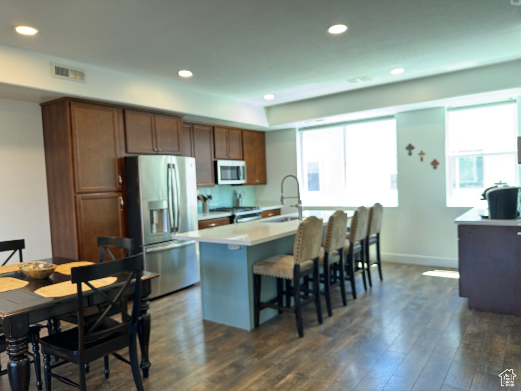 Kitchen with appliances with stainless steel finishes, a sink, dark wood-style flooring, a kitchen breakfast bar, and recessed lighting