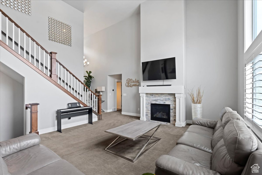 Carpeted living area featuring a high ceiling, stairway, baseboards, and a stone fireplace