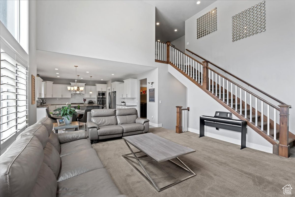 Living area featuring a high ceiling, a chandelier, light colored carpet, recessed lighting, and stairway