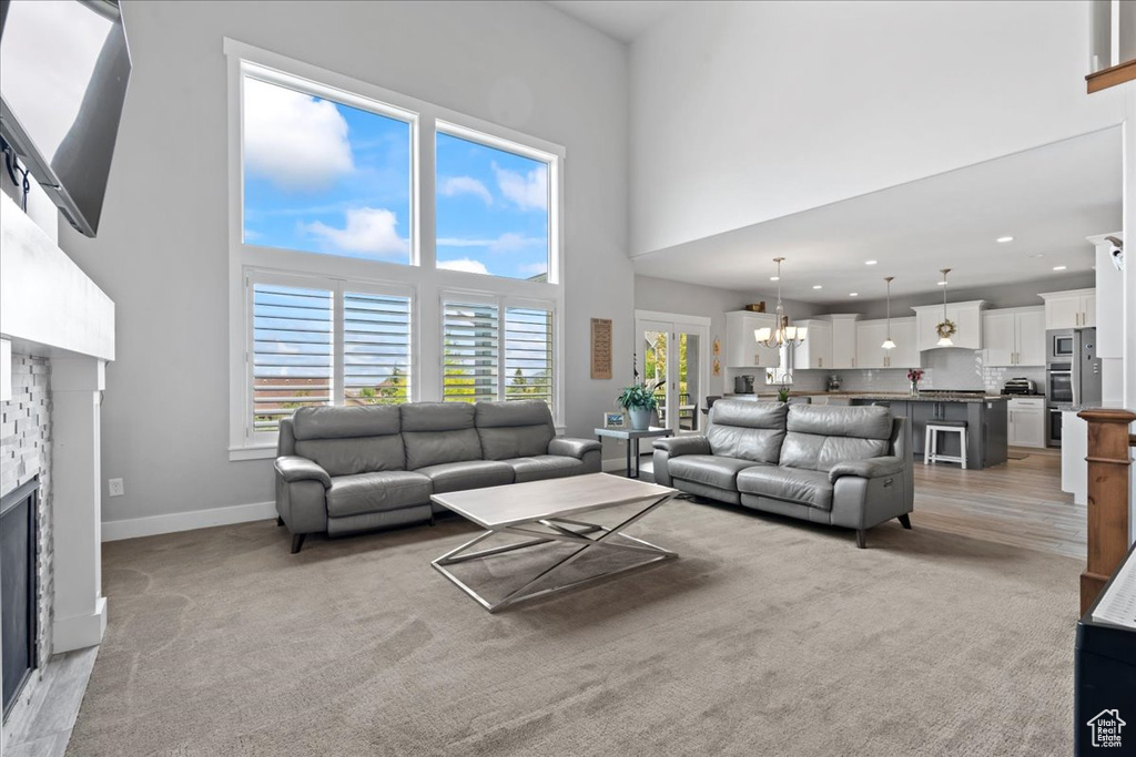 Living room with a towering ceiling, a stone fireplace, a chandelier, baseboards, and recessed lighting