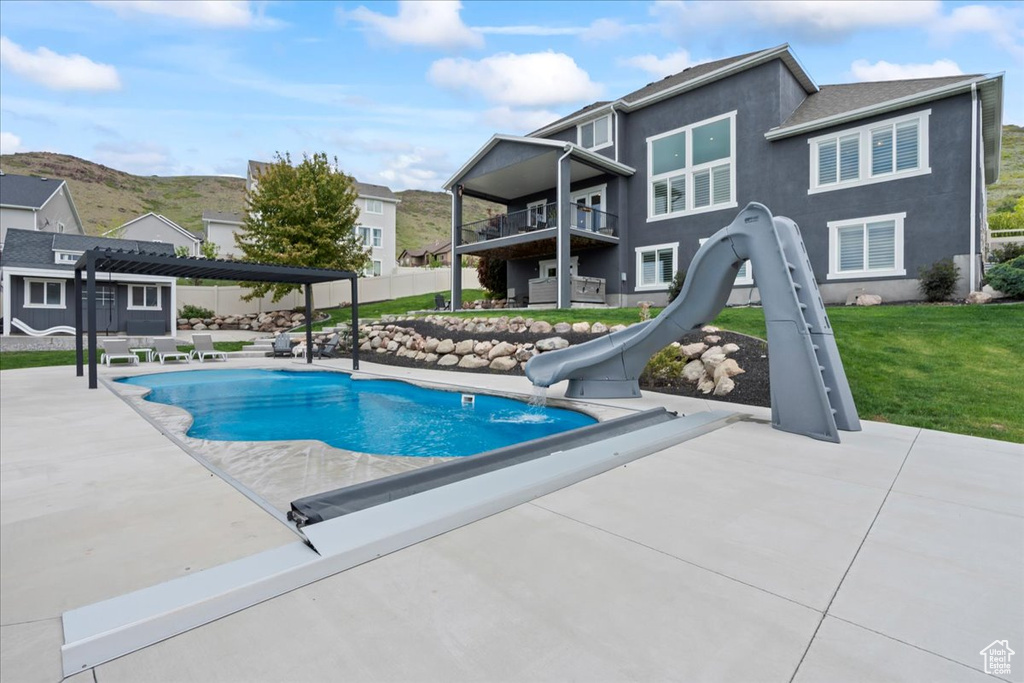 View of pool with a water slide, a pergola, a patio, and a yard