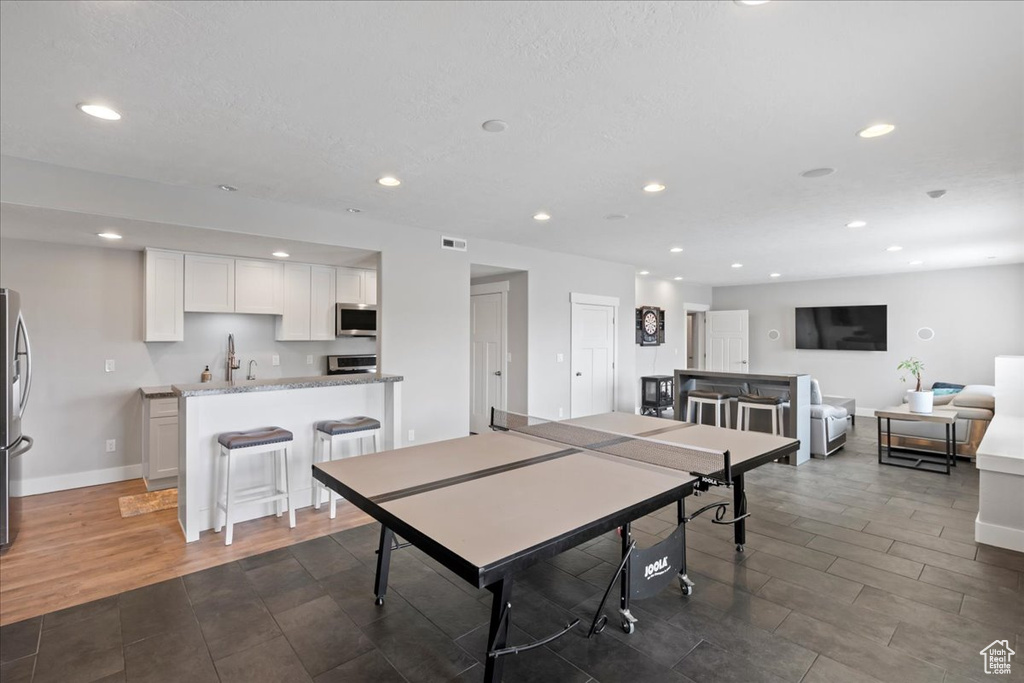 Game room with recessed lighting, bar with sink, baseboards, and dark wood finished floors
