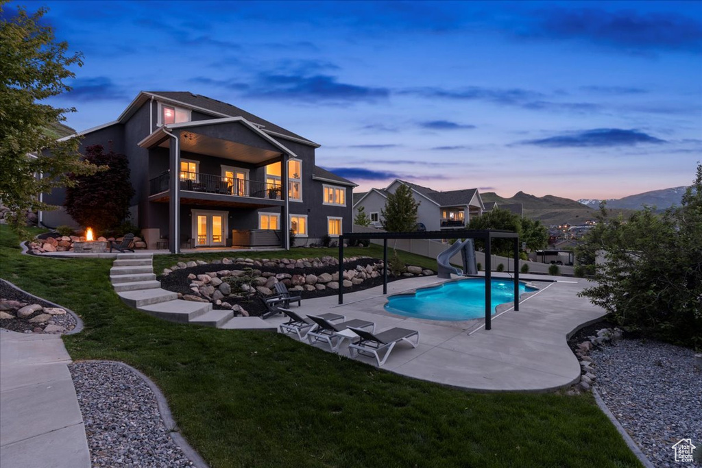 Pool at dusk featuring a water slide, a fire pit, a patio area, a lawn, and french doors