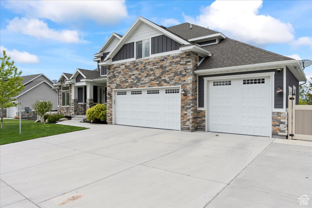 Craftsman-style home featuring stone siding, board and batten siding, concrete driveway, roof with shingles, and a front yard