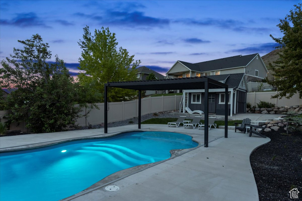Pool at dusk featuring a fenced backyard, an outbuilding, and a patio area