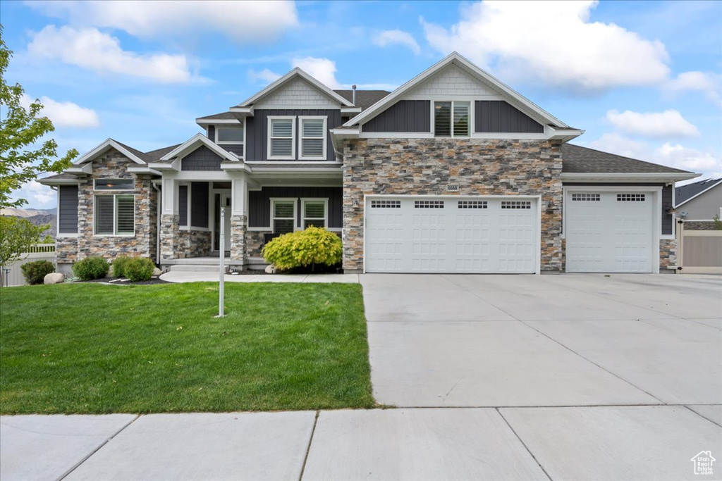 Craftsman house featuring stone siding, driveway, a front lawn, covered porch, and board and batten siding