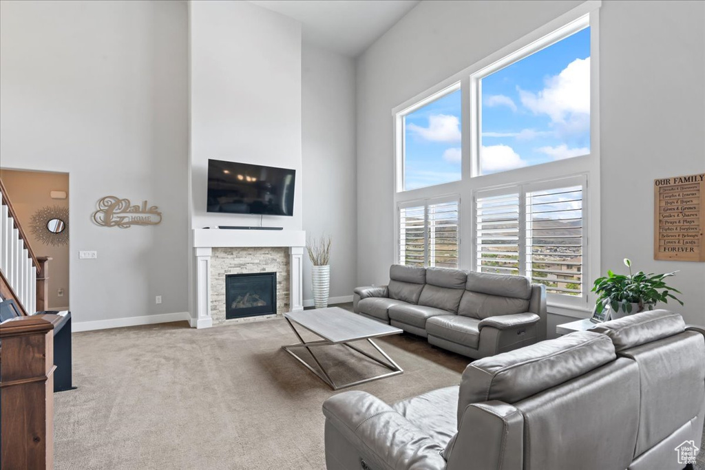 Living room featuring a high ceiling, stairway, carpet floors, baseboards, and a stone fireplace
