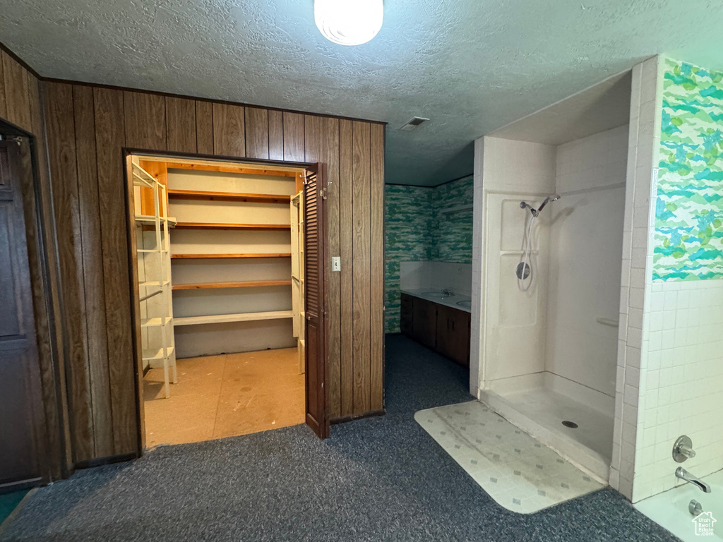 Full bathroom with a shower, a textured ceiling, a closet, and wooden walls
