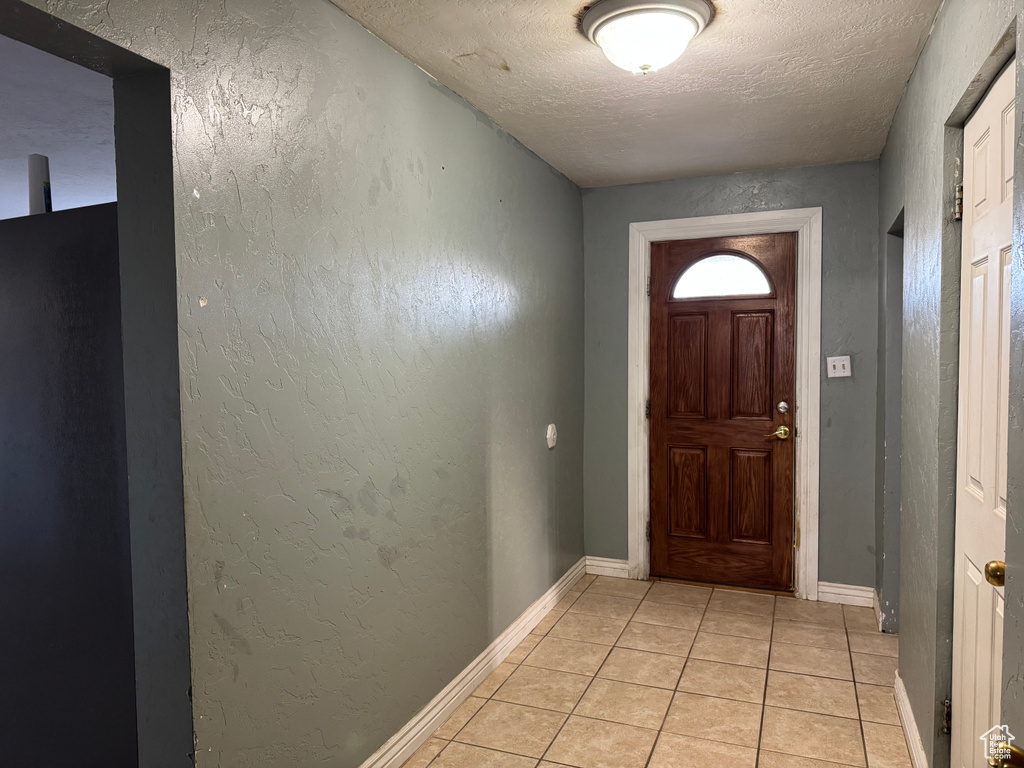Doorway to outside featuring a textured ceiling, light tile patterned flooring, baseboards, and a textured wall