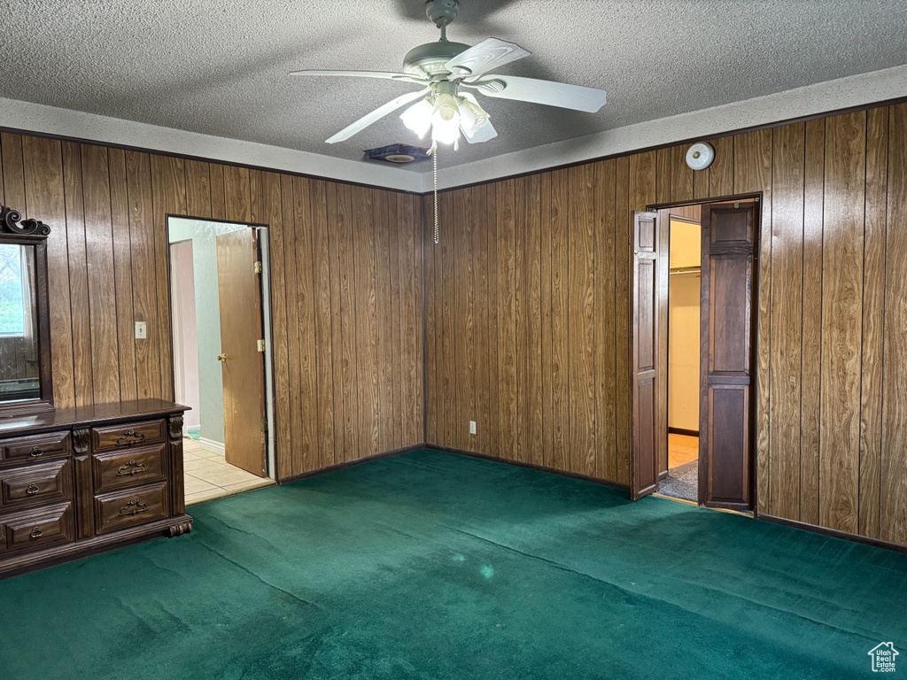 Unfurnished bedroom with light carpet, wood walls, a textured ceiling, and ceiling fan
