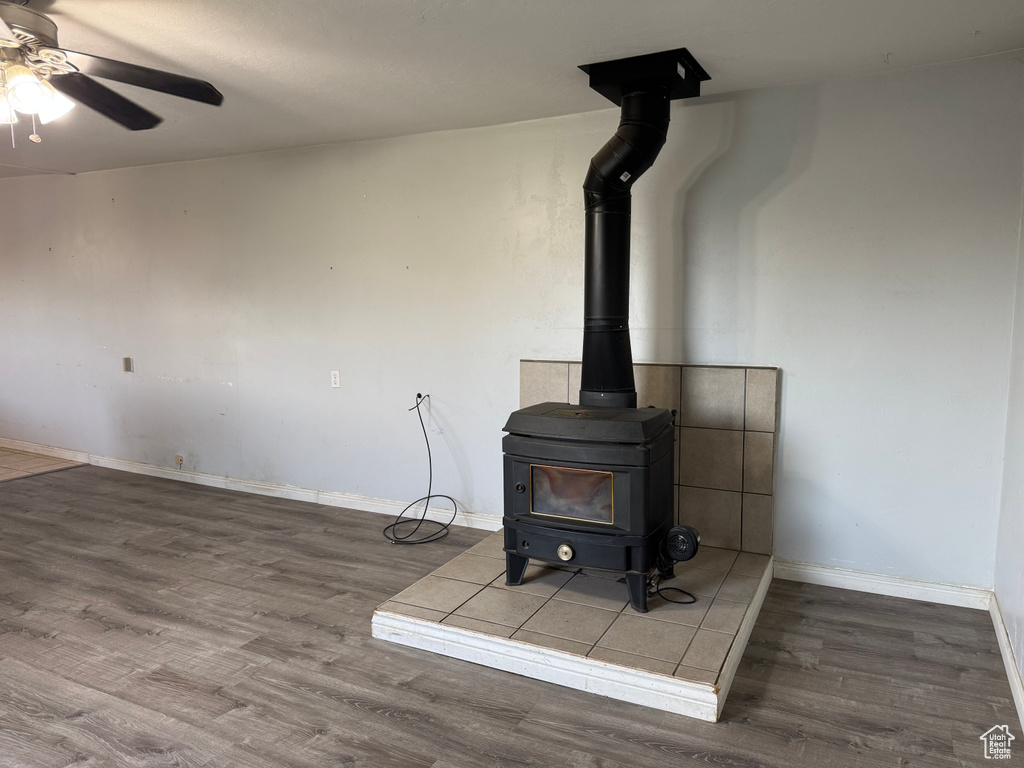 Detailed view of a wood stove, wood finished floors, ceiling fan, and baseboards