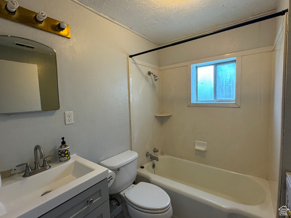 Full bathroom featuring a textured ceiling, toilet, shower / washtub combination, vanity, and a textured wall
