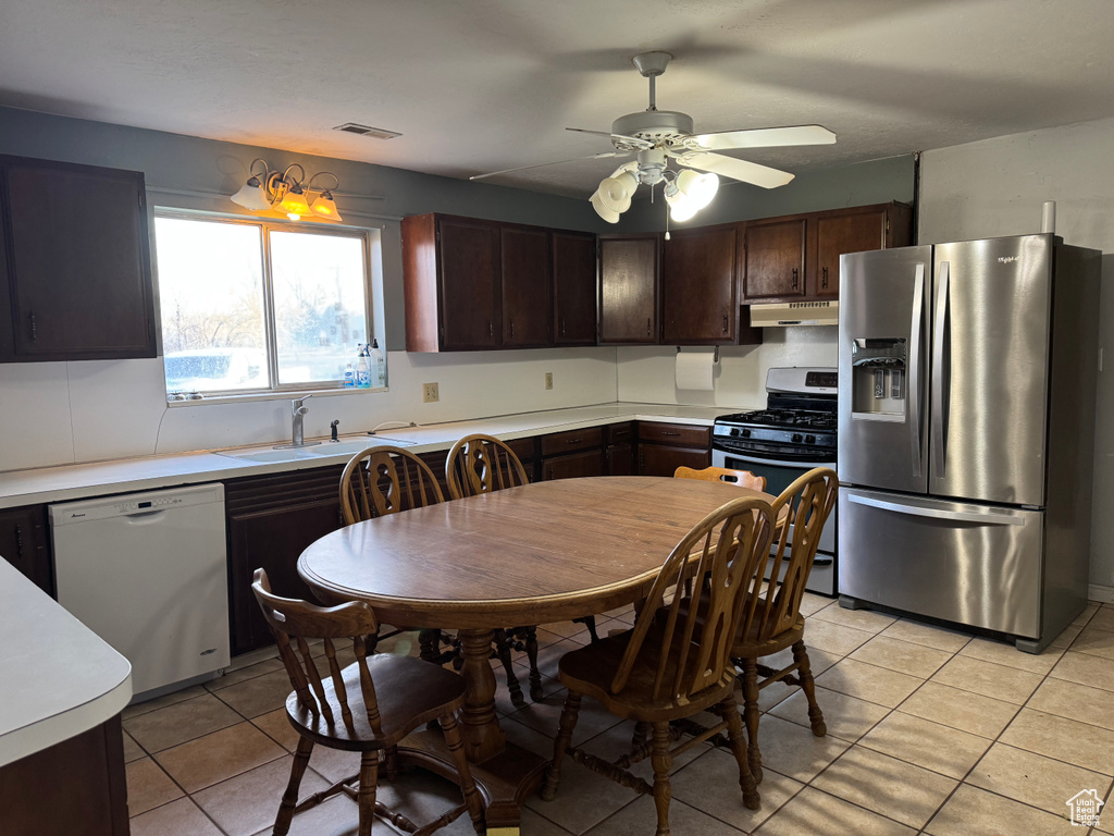 Kitchen with stainless steel appliances, a sink, under cabinet range hood, light countertops, and dark brown cabinetry