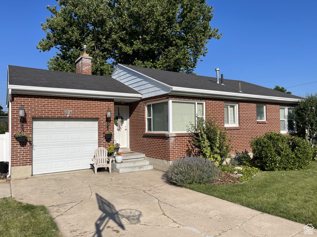 Ranch-style house featuring brick siding, a garage, driveway, a chimney, and a front lawn
