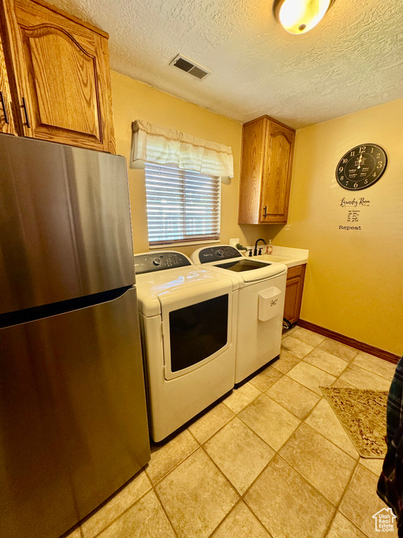Washroom with a textured ceiling, washer and clothes dryer, light tile patterned floors, a sink, and baseboards