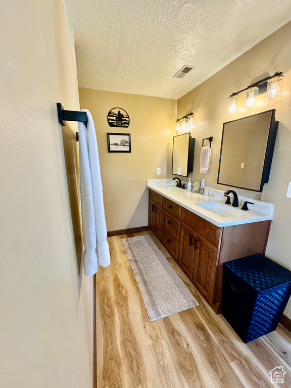 Full bath featuring wood finished floors, a textured ceiling, double vanity, and baseboards