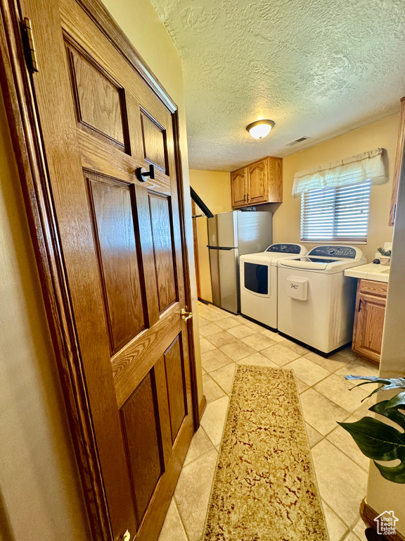 Kitchen featuring freestanding refrigerator, washer and clothes dryer, light tile patterned floors, light countertops, and a textured ceiling
