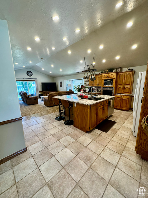 Kitchen with lofted ceiling, appliances with stainless steel finishes, open floor plan, a kitchen island with sink, and brown cabinetry
