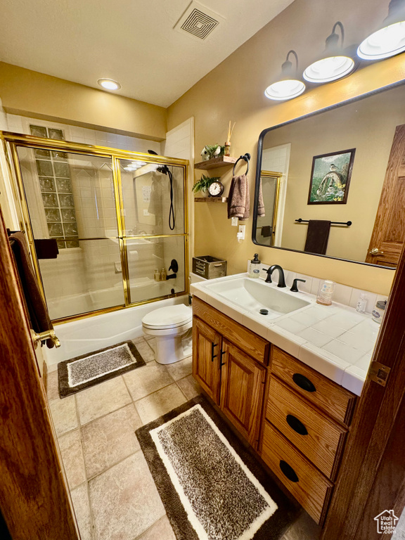 Bathroom with toilet, vanity, and bath / shower combo with glass door