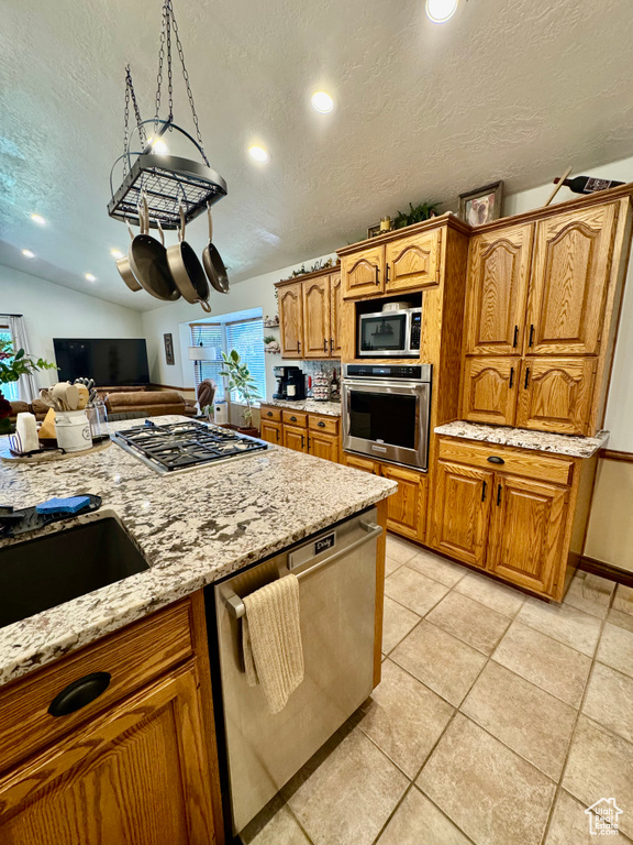 Kitchen featuring appliances with stainless steel finishes, a textured ceiling, light stone countertops, brown cabinetry, and recessed lighting