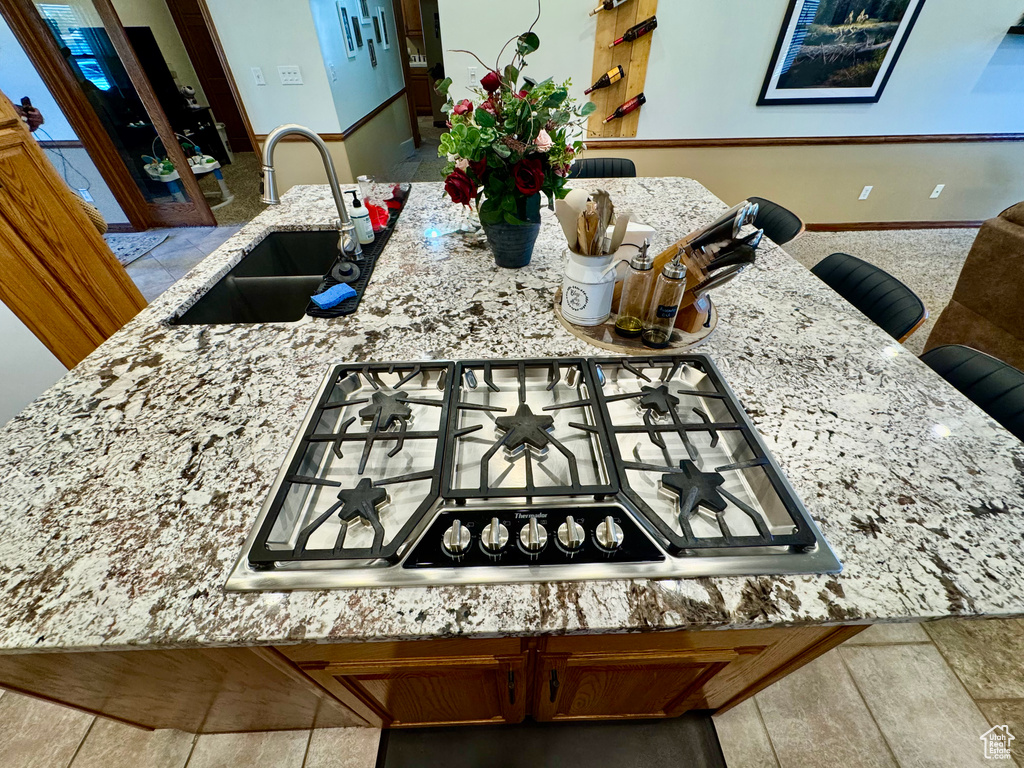 Kitchen with a sink, stainless steel gas cooktop, and light stone counters