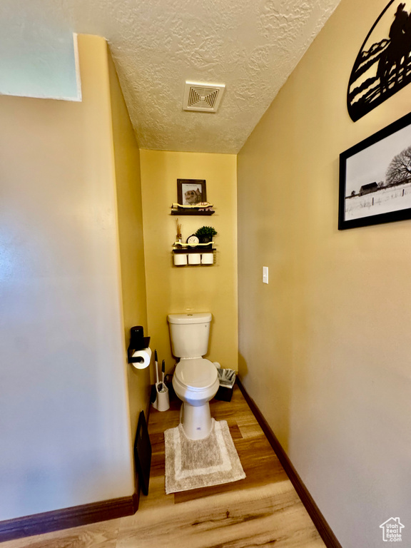 Bathroom featuring toilet, wood finished floors, a textured ceiling, and baseboards
