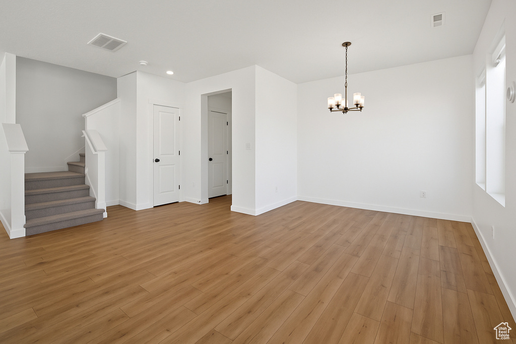 Empty room featuring a chandelier, light wood finished floors, baseboards, stairway, and recessed lighting
