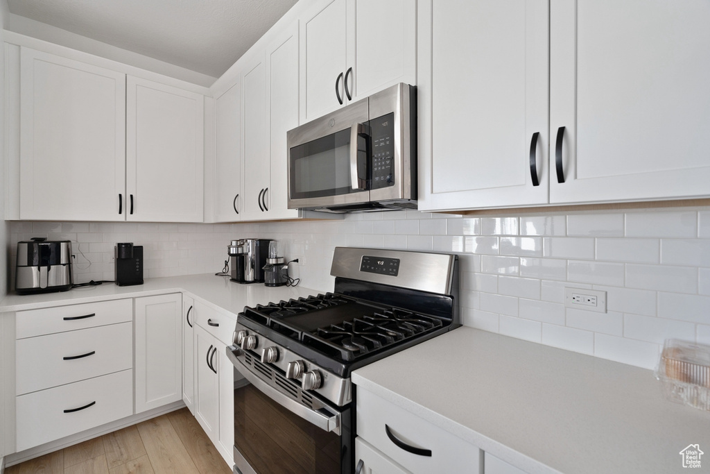 Kitchen featuring appliances with stainless steel finishes, white cabinetry, light countertops, tasteful backsplash, and light wood-type flooring