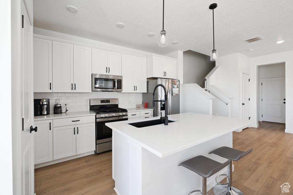 Kitchen with appliances with stainless steel finishes, decorative backsplash, a kitchen island with sink, light wood-type flooring, and a breakfast bar